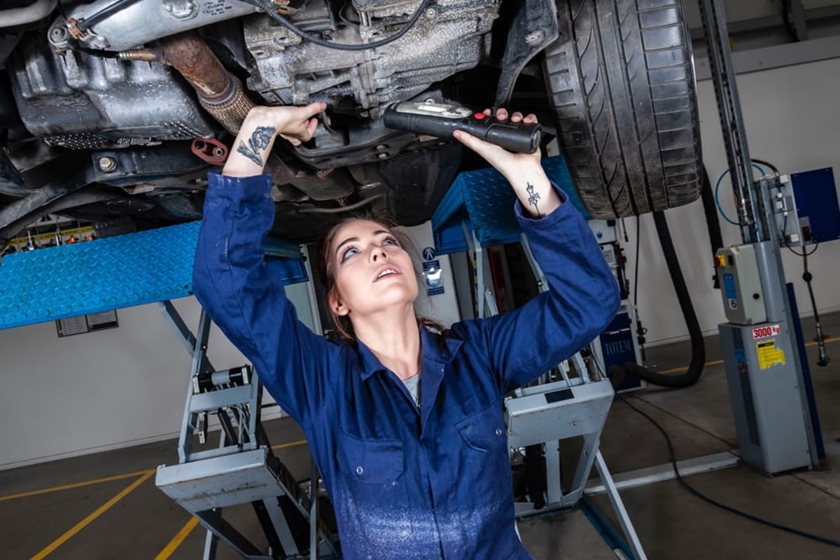 Female apprentice working underneath a car on the ramps